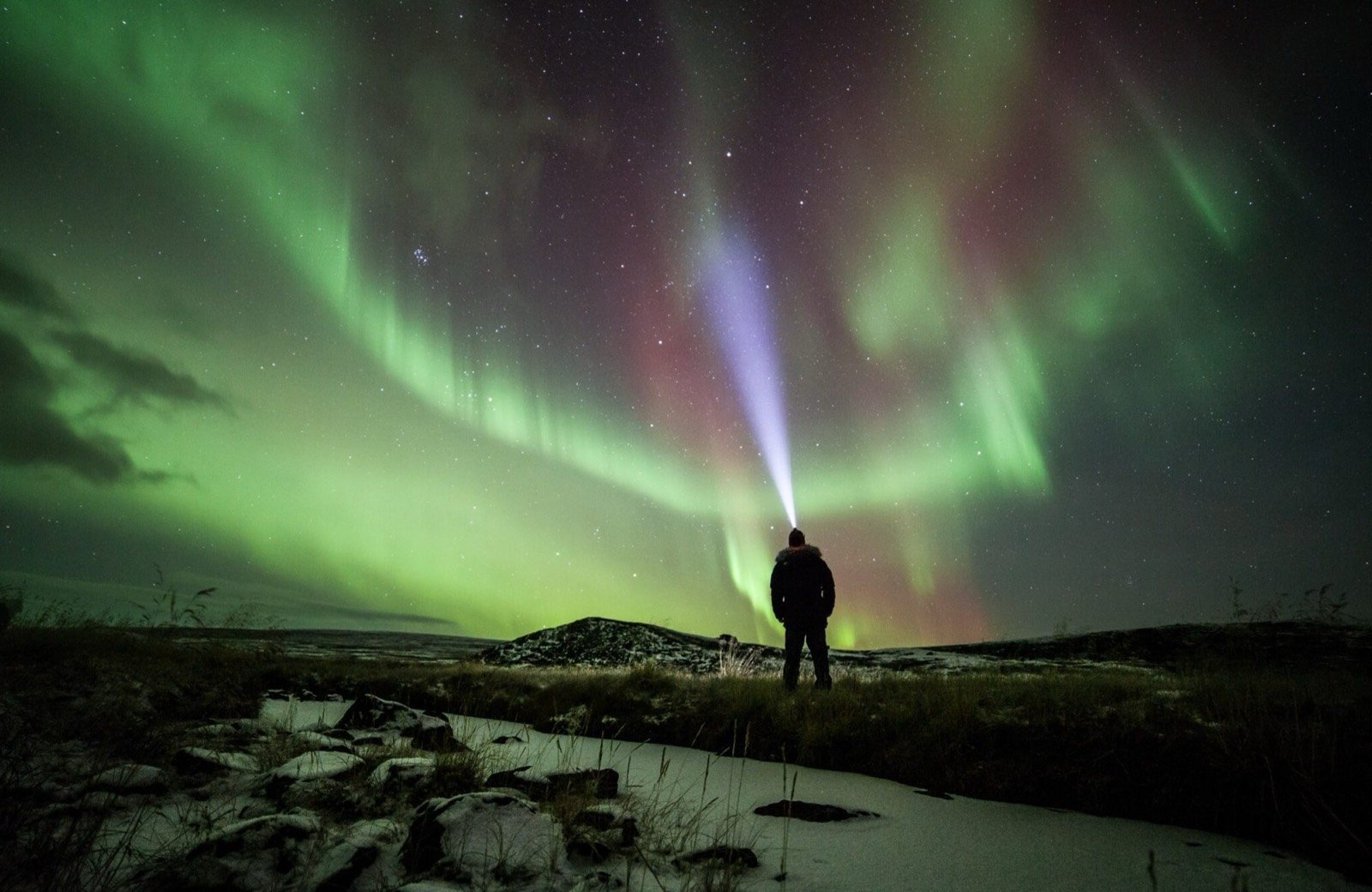 A guest with a headlamp under green Northern Lights