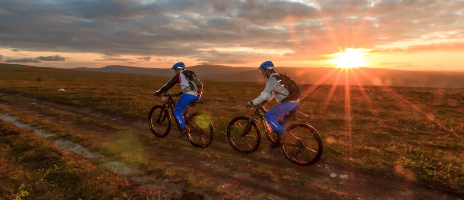 Two mountain bikers riding into the low midnight sun