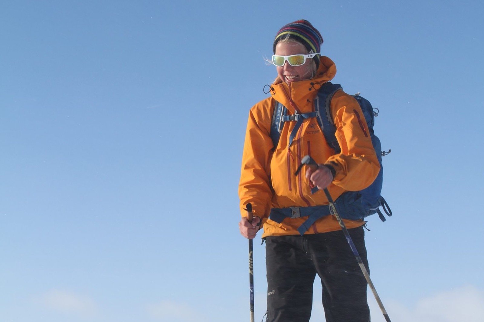 A skier in an orange jacket against a pale winter sky